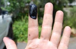 Black oil Sludge stuck to a finger, caused by dirty diesel oil built up inside engine.